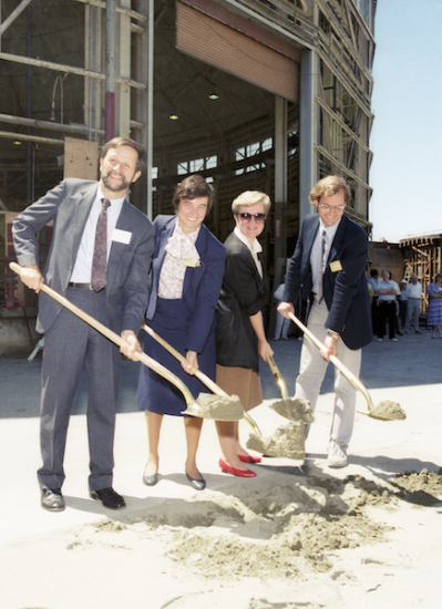 four people holding shovels in front of building under construction