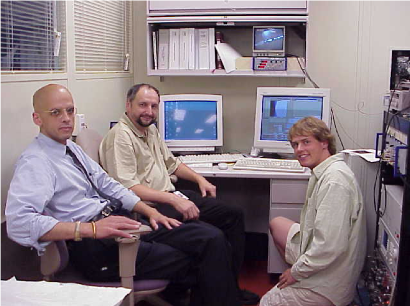 three men in front of two computer monitors
