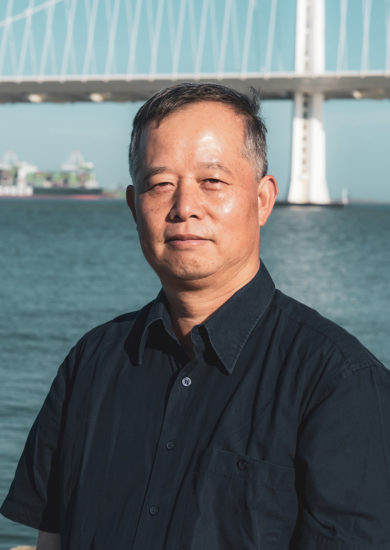 Photo of man in black shirt with Bay Bridge in background.