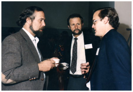 Photo of three men in suits, two of them holding coffee cups.