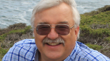 man wearing tinted glasses in front of a grassy coastline and water