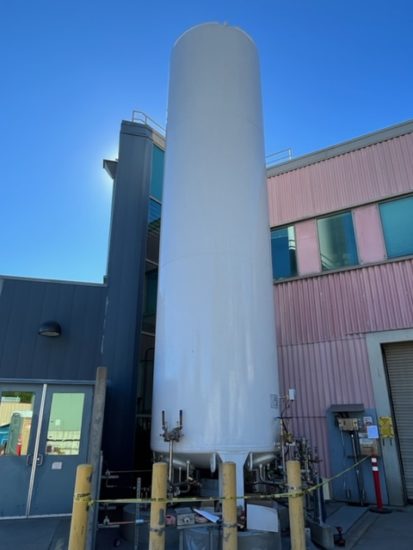 A large white cylindrical tank next to a two-story pink and grey building.