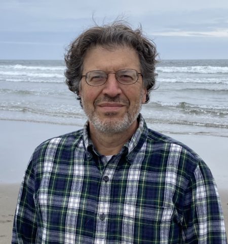A man, wearing glasses, standing at a beach.