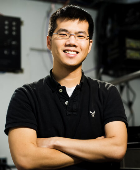 Photo of Will Chueh in black polo shirt, smiling, with arms crossed.