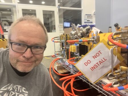A man standing next to some scientific apparatus which has a sign "do not install".