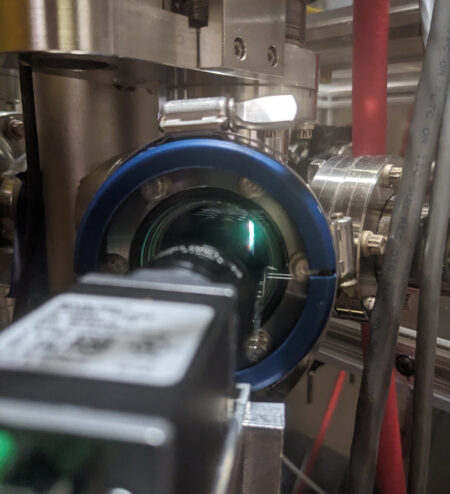 Photo of the view through a beamline viewport showing a glowing blue-white line.