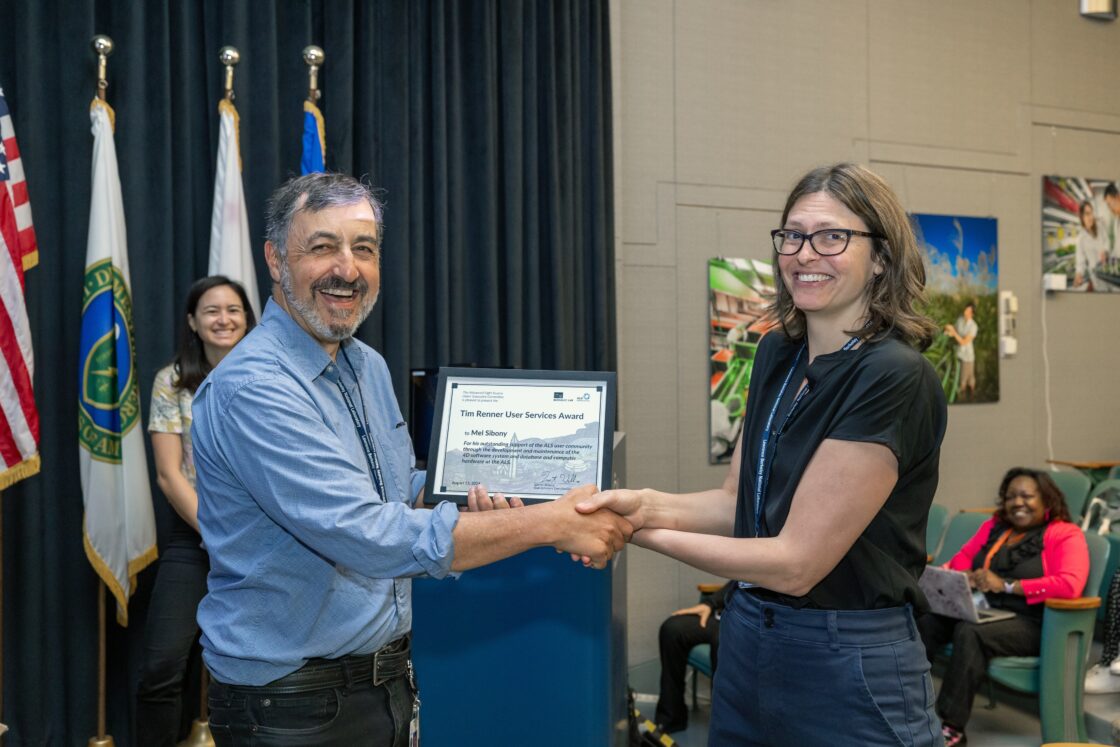 A woman handing a man an awards certificate and shaking his hand. Both are smiling happily.