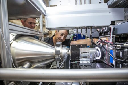 Two people looking at a sychrotron beamline to study the components of viruses responsible for replication, immune system evasion, and protein production, as well as studying nanoparticles used for mRNA delivery in vaccines.