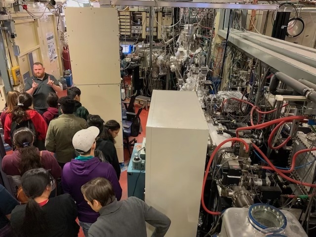 a man standing next to scientific equipment facing a group of people