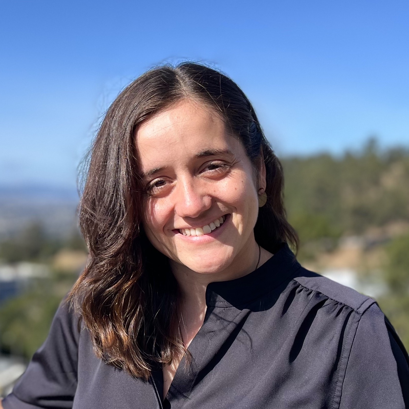 woman smiling in front of blue sky and green trees