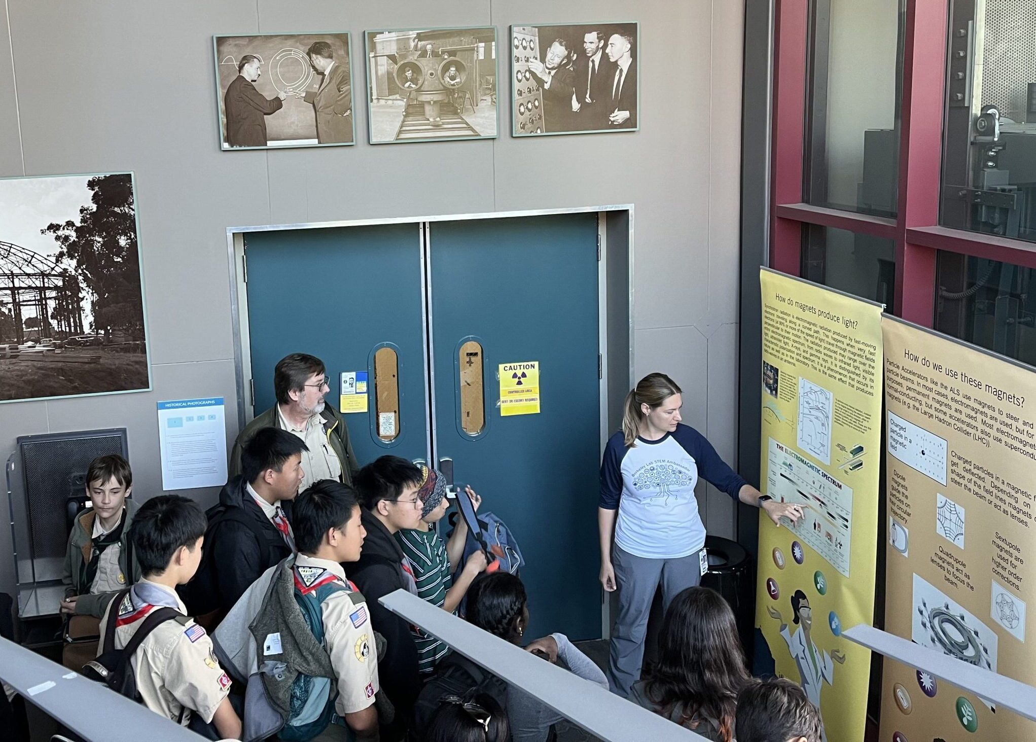 Female scientist giving a tour to middle school aged students and pointing at an illustration on a poster.