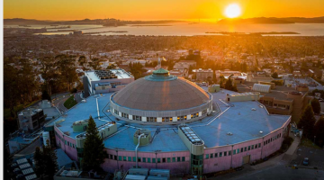 A dome-shaped building with a sunset and a Bay behind it.