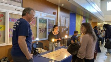 Three people standing around a table with a display talking animatedly.