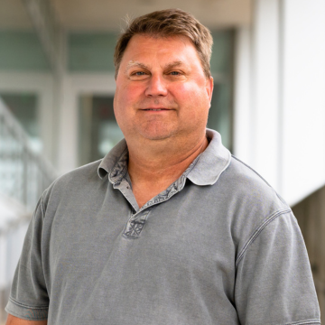 Person with short blond hair and a grey polo shirt.