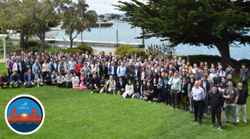Large group of people standing in front of marina with boats and a logo that has a bridge in it and the name ICESS.
