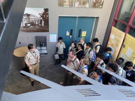 An adult in a scout uniform talking to a four of teenaged scouts.