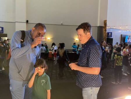 An adult and a child looking through diffraction gratings while another adult talks to them.