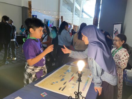 A adult and a child standing across each other on opposite sides of a table. The adult is giving instructions.