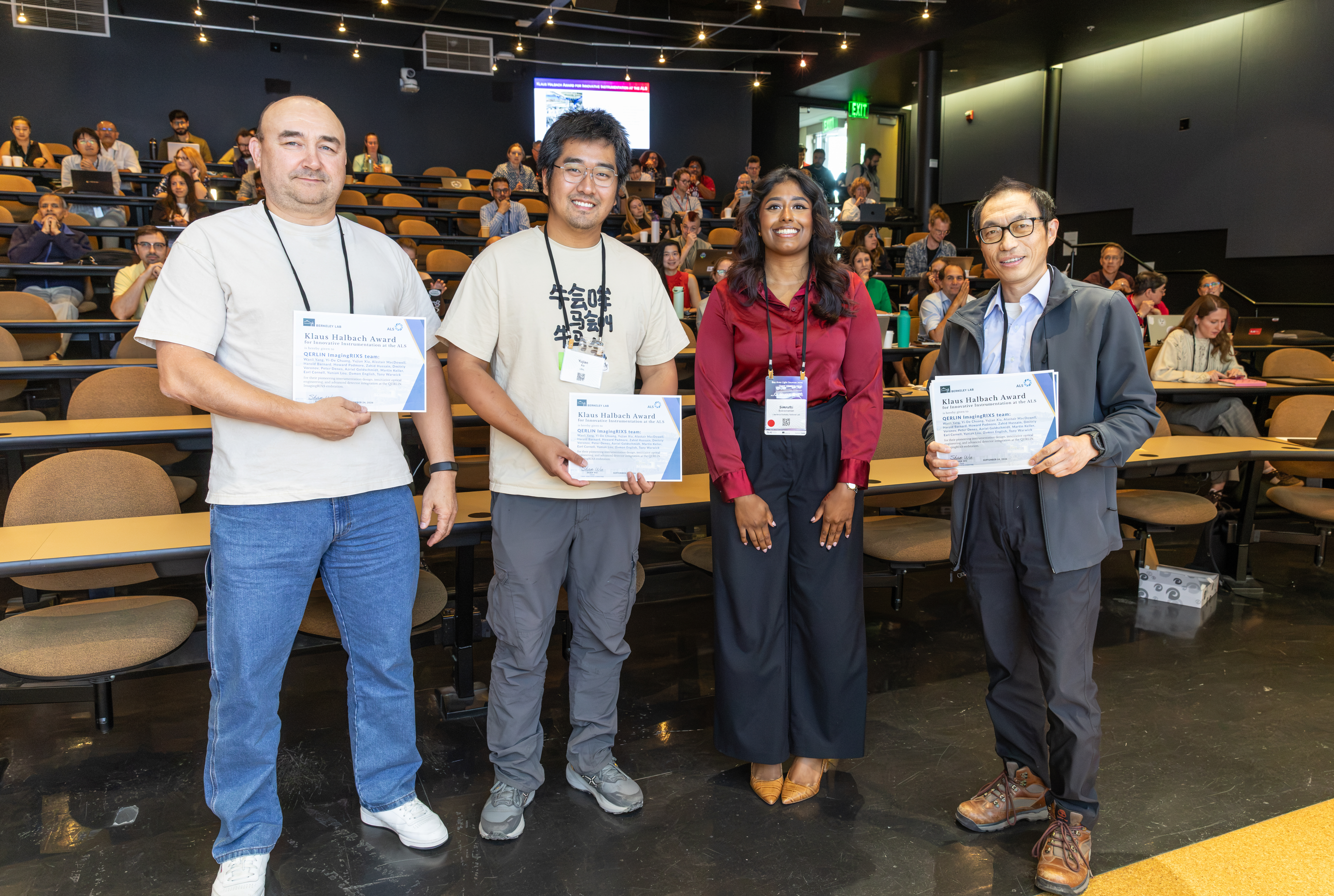 three people accept award certificates from a presenter in a large presentation room 